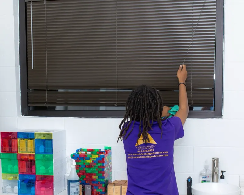 Ascent Cleaning Solutions team member in branded uniform cleaning blinds in a Nashville daycare